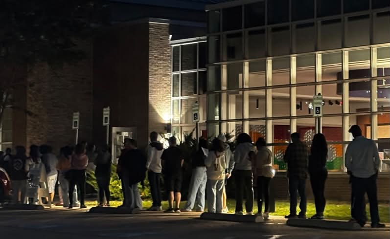 Voters standing in a long line outside a library at dusk